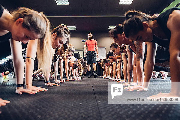 Große Gruppe von Frauen trainiert in Turnhalle mit männlichem Trainer  in Reihen  die Liegestützen machen