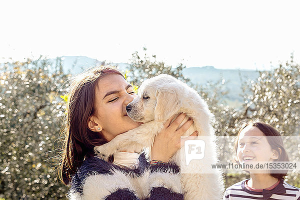 Mädchen mit ihrer Freundin hält einen süßen Golden Retriever-Welpen im Obstgarten hoch  Scandicci  Toskana  Italien