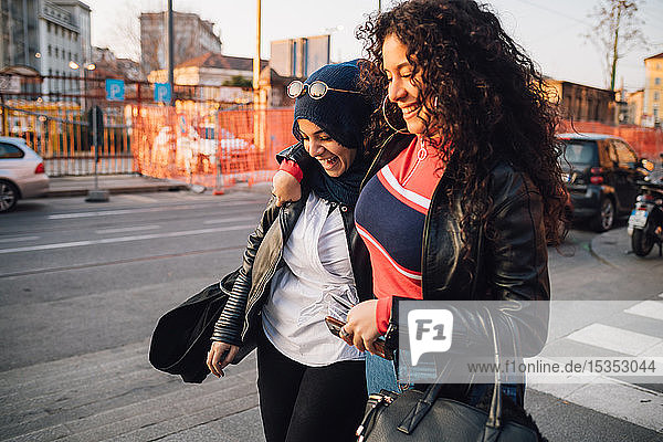 Young woman in hijab and best friend walking and talking in city