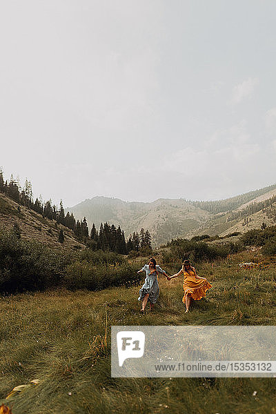 Two women holding hands running in rural valley  Mineral King  California  USA