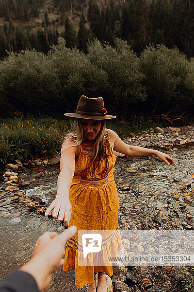 Schwangere Frau in orangefarbenem Maxikleid, die aus ländlichem Fluss nach der Hand greift, Mineral King, Kalifornien, USA