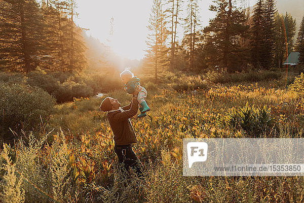 Mittelgroßer erwachsener Mann hält Kleinkind-Tochter im ländlichen Tal bei Sonnenuntergang hoch  Mineral King  Kalifornien  USA