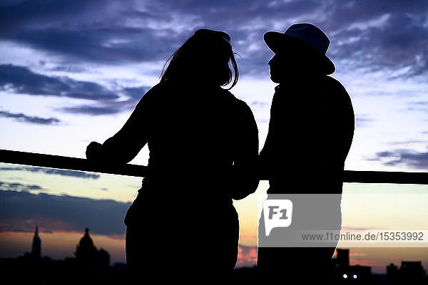 Silhouetted couple stands at a railing overlooking the skyline of Havana at sunset; Havana  Cuba