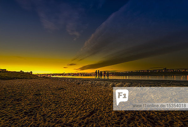 Silhouette einer Familie mit drei Kindern am Ufer des Flusses Tyne bei Sonnenuntergang  im Vordergrund ein Strand; South Shields  Tyne and Wear  England
