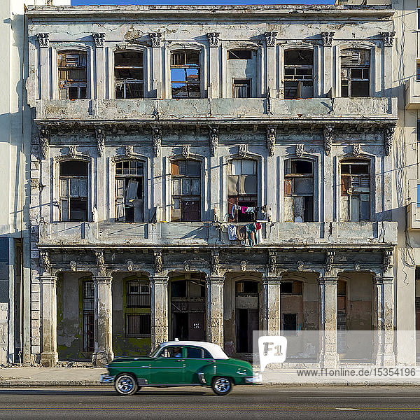 An old car passes the weathered facade of old buildings along a street; Havana  Cuba