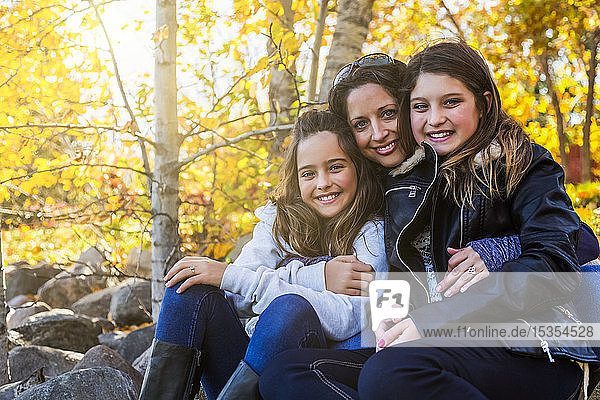 A mother and her two daughters posing for a family portrait in a city park on a warm fall day; Edmonton  Alberta  Canada