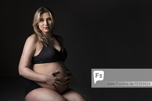 A young pregnant woman holding her belly in a studio and posing for the camera: Edmonton  Alberta  Canada