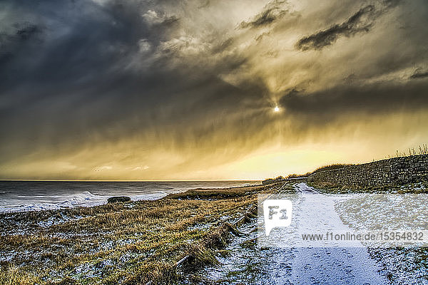 Schneebedeckter Weg entlang der Küstenlinie mit goldenem Sonnenlicht  das die Wolken beleuchtet; South Shields  Tyne and Wear  England