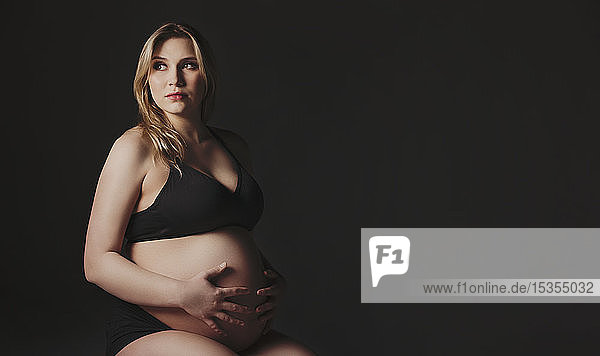 A young pregnant woman holding her belly in a studio and looking away from the camera thinking about her unborn child: Edmonton  Alberta  Canada