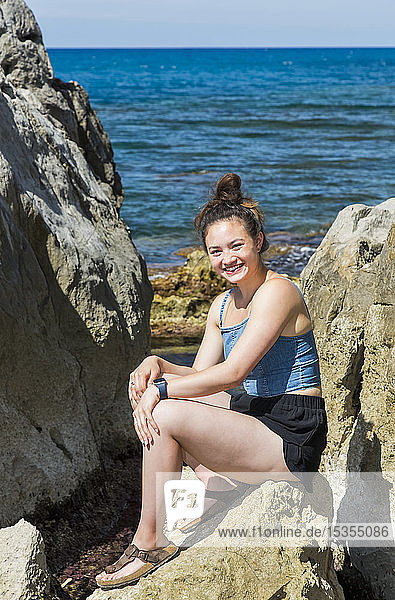 Eine junge Touristin sitzt auf einem Felsen an der Mittelmeerküste; Cefalu  Sizilien  Italien