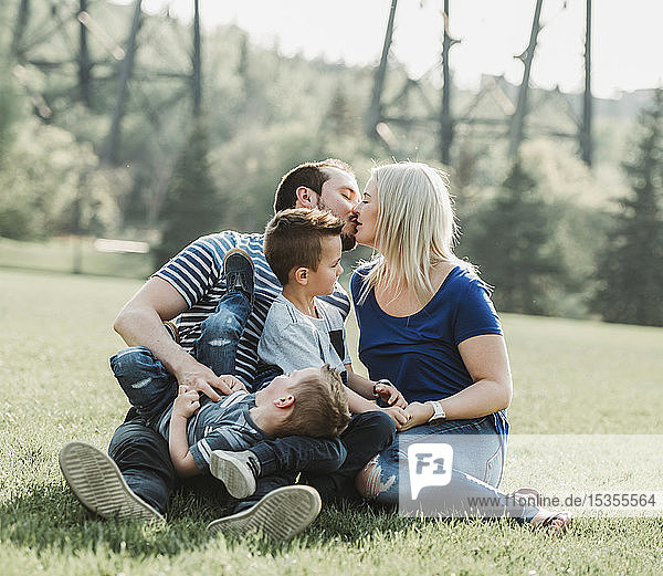Eine Familie mit kleinen Kindern  die in einem Park spielen  wobei sich die Mutter und der Vater küssen; Edmonton  Alberta  Kanada