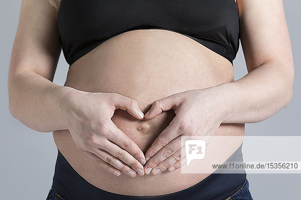 Eine junge schwangere Frau  die in einem Studio ihren Bauch hält und ein Herz über ihrem ungeborenen Kind formt; Edmonton  Alberta  Kanada