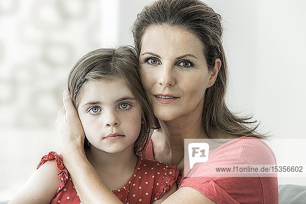Mother and daughter sit together on the couch and look into the camera  mother holds protective hand around daughter  Germany  Europe
