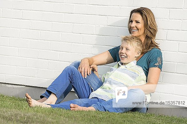 Mutter und Sohn sitzen zusammen vor einer weißen Wand  schauen in die Ferne  lächelnd  Deutschland  Europa