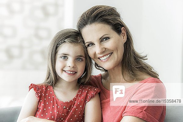 Mother and daughter sit together on the couch and look into the camera  smile  Germany  Europe