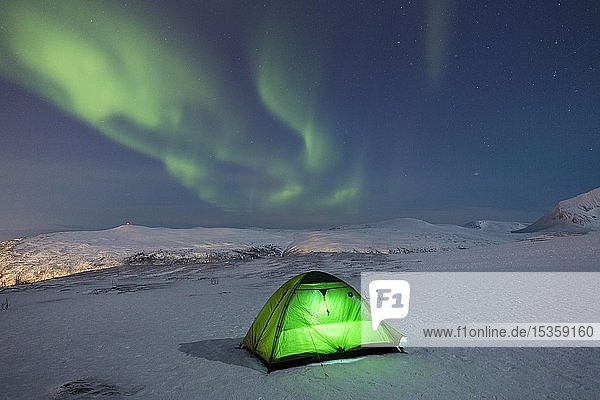 Grün beleuchtetes Zelt im Schnee und Polarlicht über dem Fjellheisen Tromsö Norwegen Europa