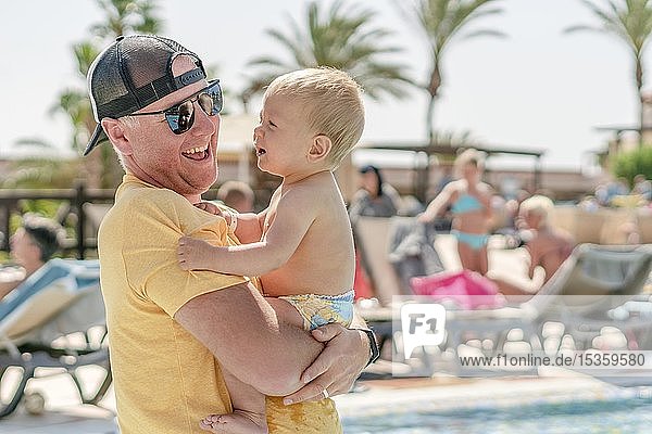 Happy father holding his cheerful son on holiday  resort with pool and palm trees as background  Portugal  Europe