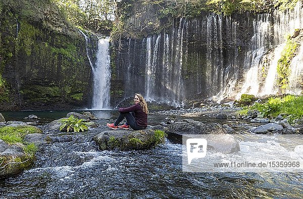 Young woman sitting on a stone in a river  Shiraito Waterfall  Yamanashi Prefecture  Japan  Asia