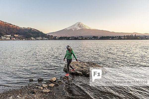 Evening mood  Young woman walks over stones in the water  view over Lake Kawaguchi  back volcano Mt. Fuji  Yamanashi Prefecture  Japan  Asia