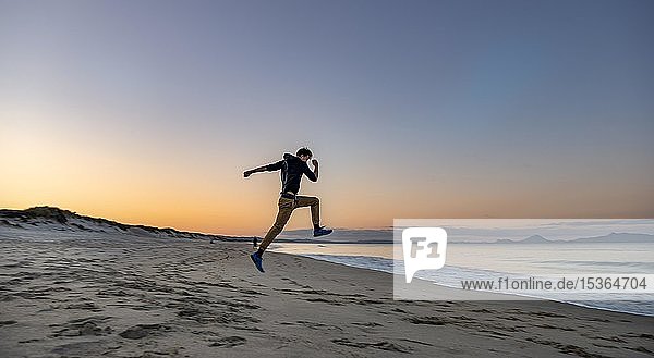 Junger Mann springt in die Luft  Strand Waipu Beach bei Sonnenuntergang  Waipu Cove  Northland  Neuseeland  Ozeanien
