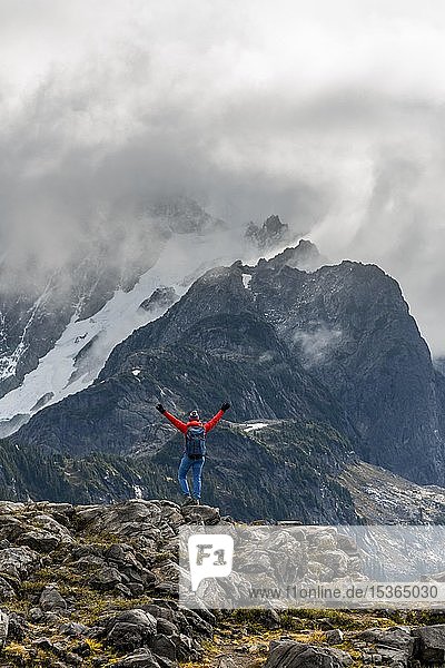 Female hiker stretches arms into the air  view of Mt. Shuksan with snow and glacier  cloudy sky  Mt. Baker-Snoqualmie National Forest  Washington  USA  North America