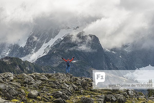 Female hiker stretches arms into the air  view of Mt. Shuksan with snow and glacier  cloudy sky  Mt. Baker-Snoqualmie National Forest  Washington  USA  North America