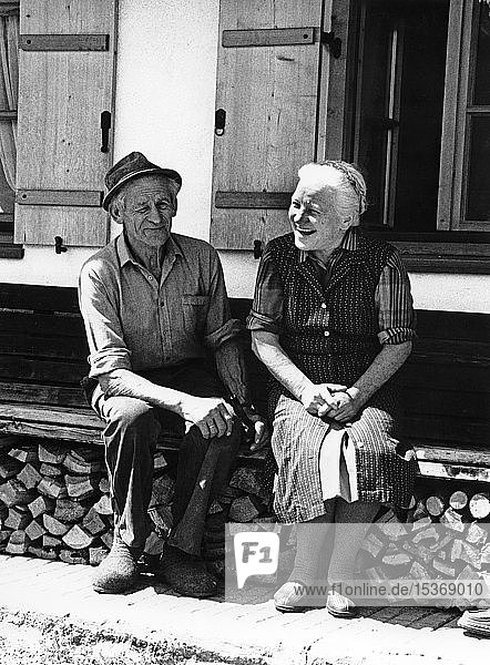 Altes glückliches Paar auf der Hausbank vor dem Bauernhof  Schuhmacher Cajetan Anker mit seiner Frau Resi  um 1960  Oberaudorf  Oberbayern  Bayern  Deutschland  Europa