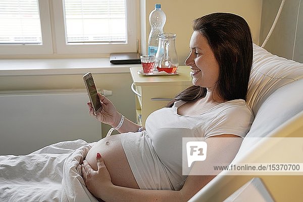Risikoschwangerschaft  schwangere Frau liegt auf einem Entbindungsbett im Krankenhaus und schaut auf ein Mobiltelefon  Karlovy Vary  Tschechische Republik  Europa