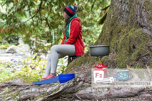 Kochen im Freien mit Campingkocher und Campingutensilien  im Freien  junge Frau sitzt daneben  Mt. Baker-Snoqualmie National Forest  Washington  USA  Nordamerika