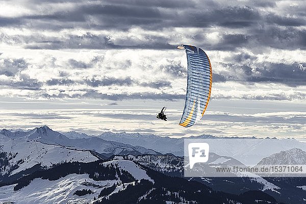 Gleitschirmfliegen in der Luft vor einer schneebedeckten Alpenkette im Winter  Brixen im Thale  Tirol  Österreich  Europa