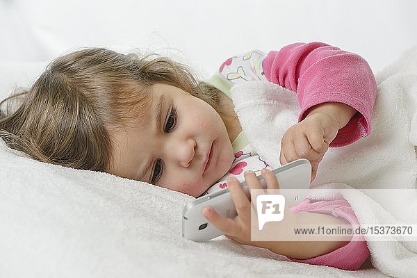 Girl  2 years  portrait  lying with mobile phone  Germany  Europe
