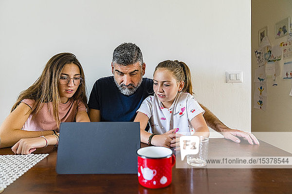 Vater mit zwei Töchtern betrachtet Tafel auf Holztisch zu Hause