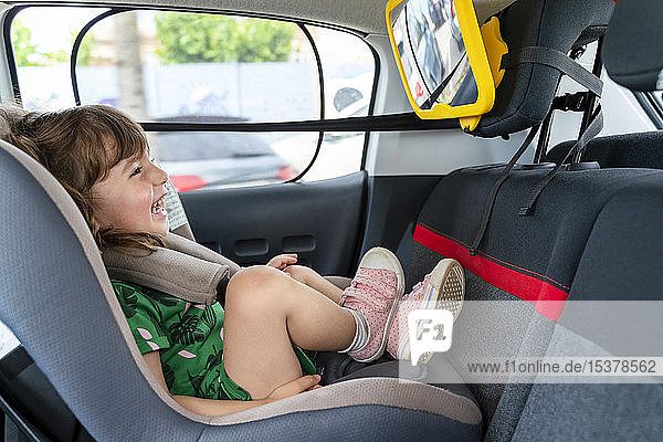 Laughing toddler girl sitting in a car seat looking in a mirror