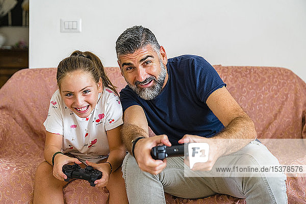 Father and daughter playing video game on couch at home