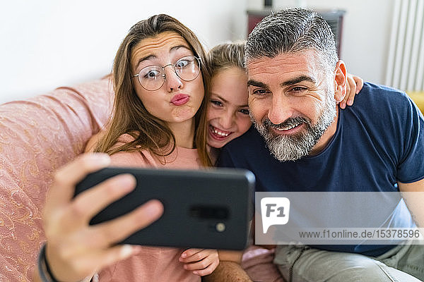 Happy father with two daughters taking selfie on couch at home