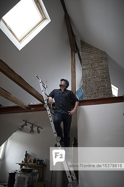 Architekt auf der Baustelle eines Dachgeschossausbaus  stehend auf einer Leiter