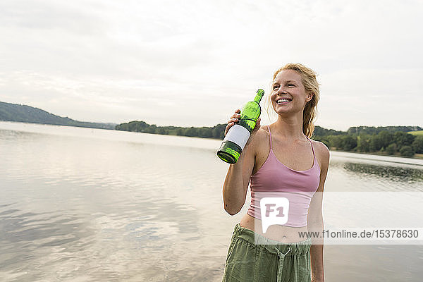 Glückliche junge Frau trinkt Wasser an einem See