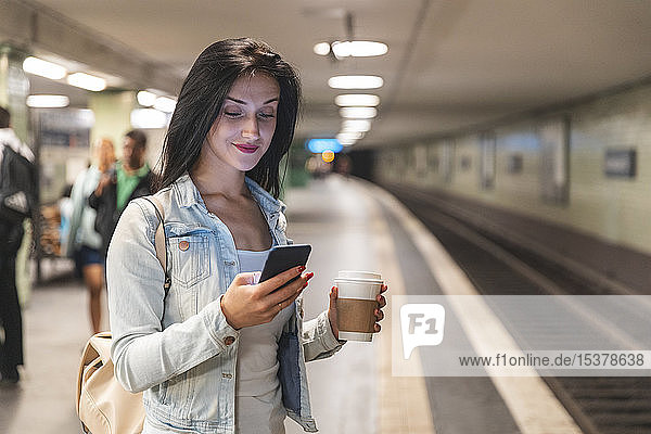 Young woman with cell phone at metro station waiting for the train  Berlin  Germany