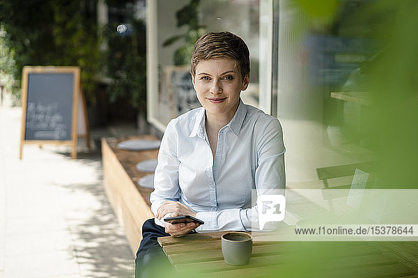 Porträt einer lächelnden Geschäftsfrau mit Handy in einem Cafe