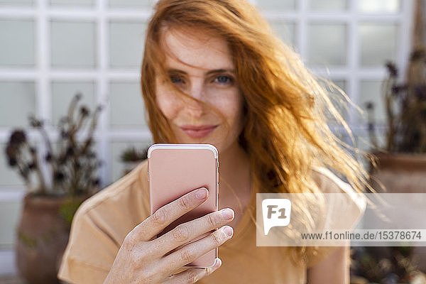 Hand of smiling redheaded young woman holding cell phone  close-up
