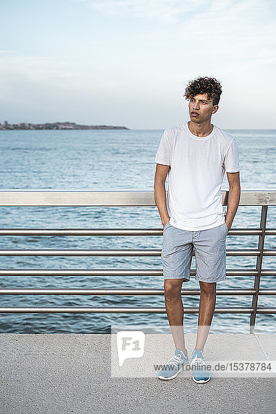 Young man standing on bridge by the sea  with hands in pockets