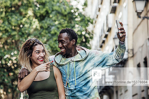 Porträt eines lachenden Paares  das sich mit einem Smartphone selbstständig macht  Madrid  Spanien