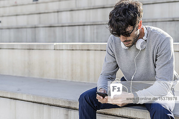 Mann sitzt auf einer Außentreppe und benutzt ein Smartphone