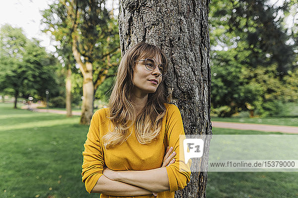 Junge Frau an einem Baum im Park mit seitlichem Blick