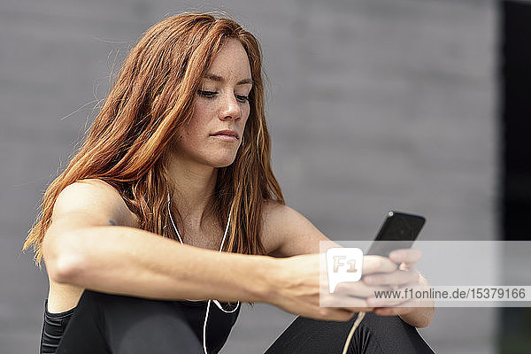 Sporty young woman with earphones having a break using smartphone outdoors