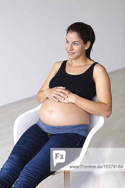 Junge schwangere Frau sitzt auf einem Stuhl und denkt über die Zukunft nach