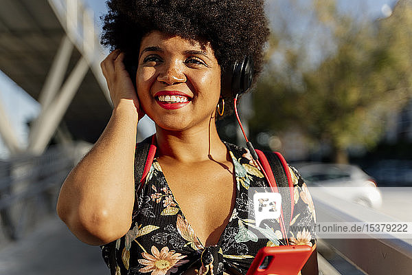 Weibliche Afroamerikanerin mit Kopfhörern und Smartphone  die Musik hört und zur Seite schaut