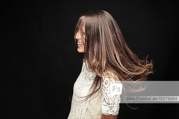 Glückliche junge Frau mit langen braunen Haaren vor schwarzem Hintergrund