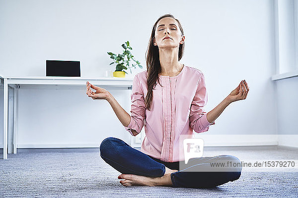 Junge Frau meditiert im Büro auf dem Boden