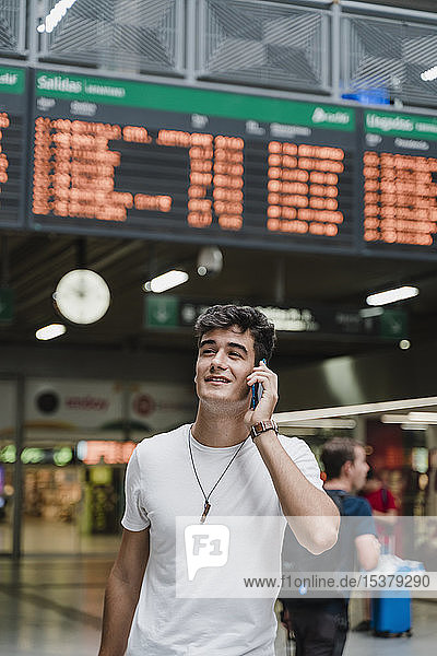 Junger Mann wartet am Bahnhof und benutzt Smartphone